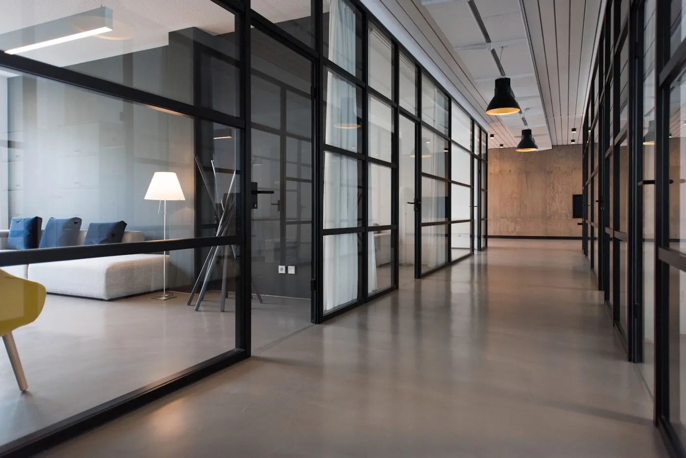 Couloir de bureaux moderne aux parois vitrées, ambiance sombre et épurée